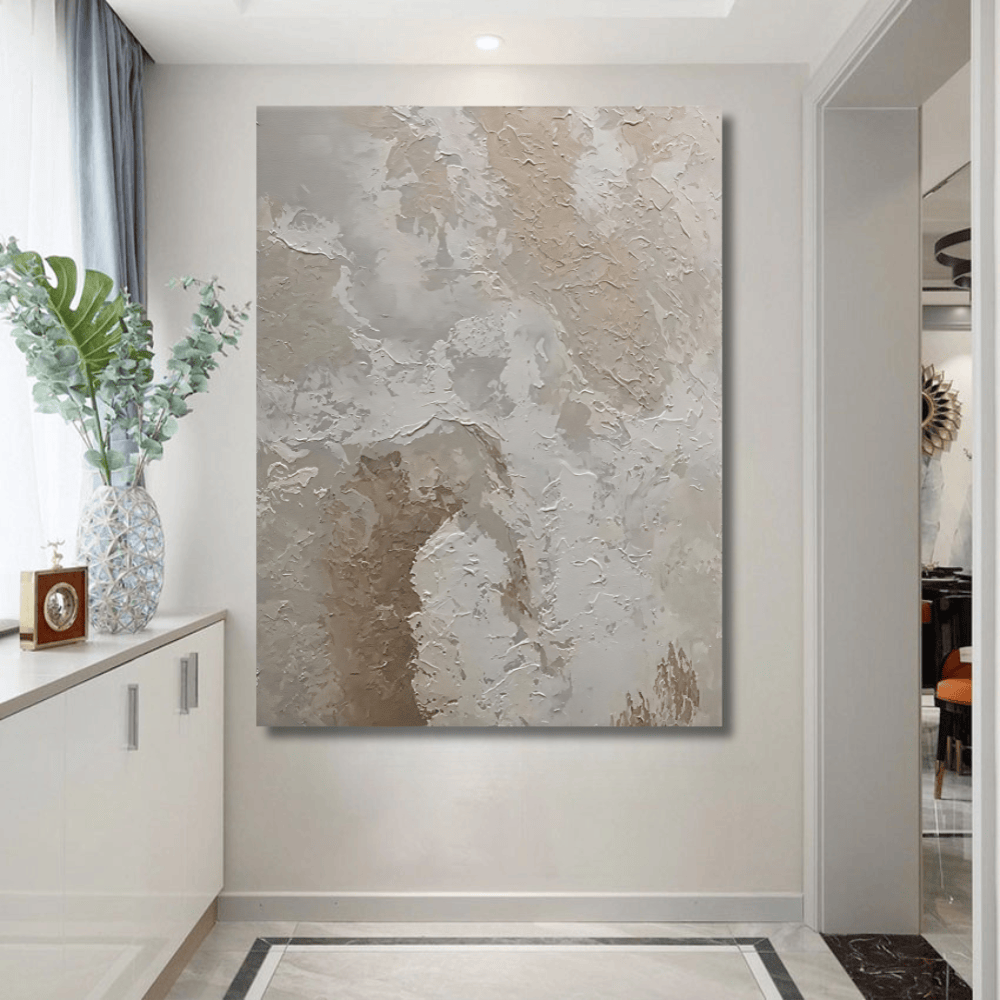Beige abstract painting wall art in a white frame hanging in a modern entryway with a plant