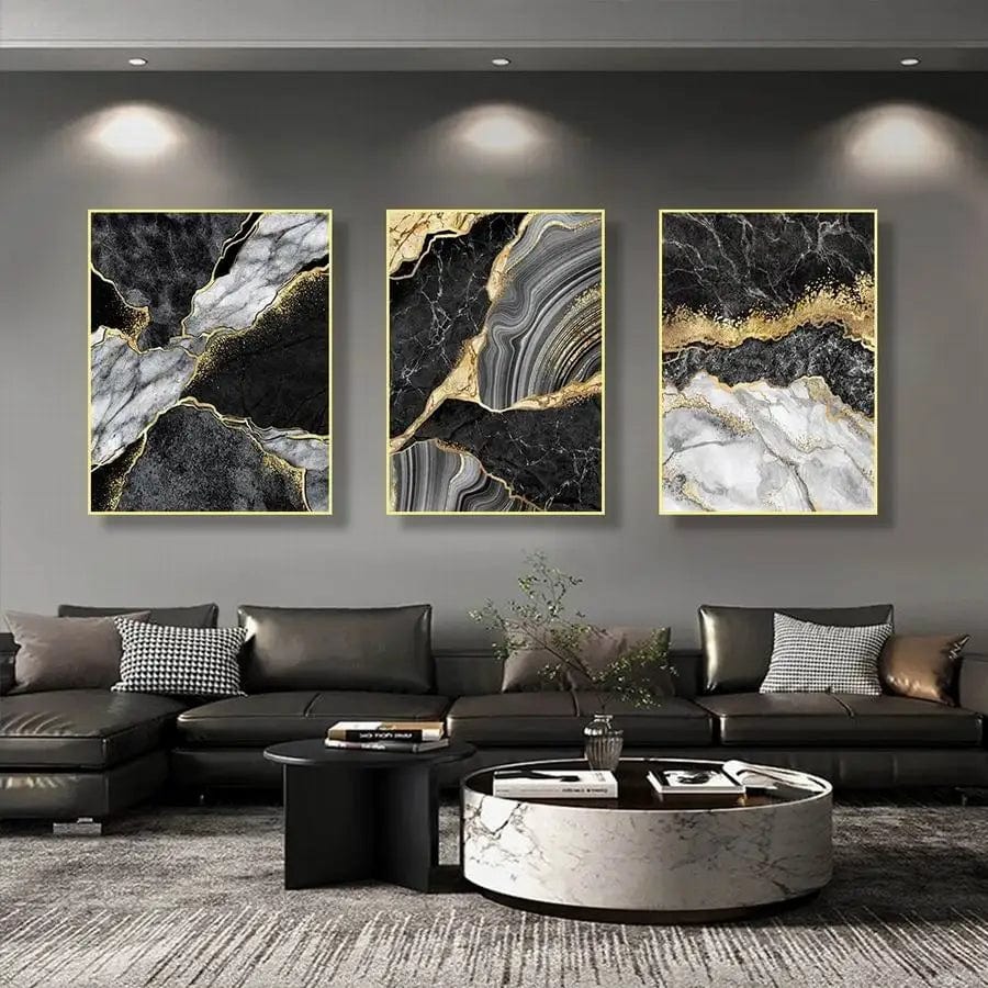 Black and gold abstract marble wall art trio in thin gold frames hanging above a grey leather sofa in a living room
