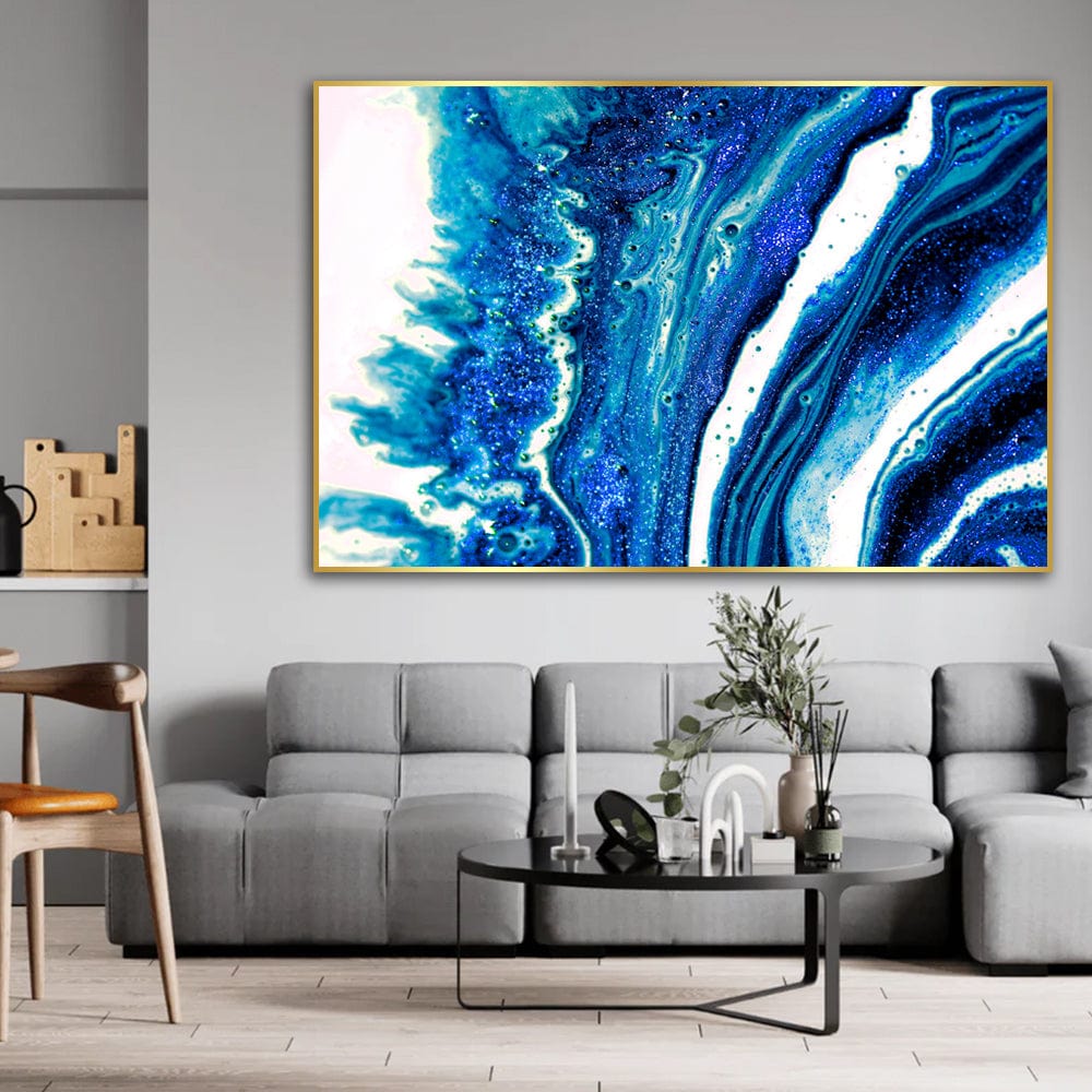 Ocean Inkscape abstract blue landscape wall art, fluid cobalt and white waves in a thin gold frame above a gray sofa