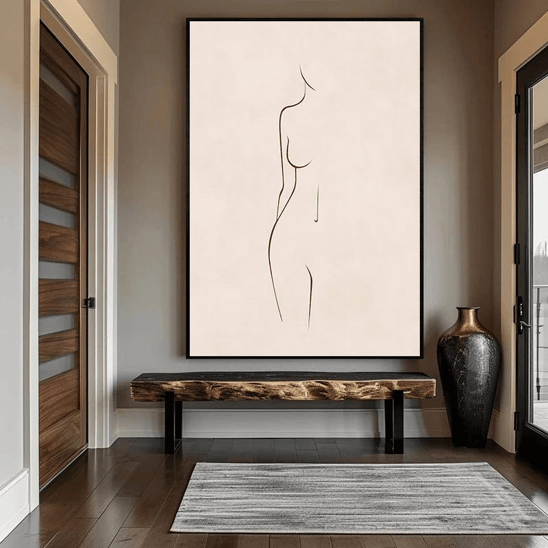 Minimalist female figure line wall art, brown silhouette on neutral background in a black frame above a wooden bench in an entryway