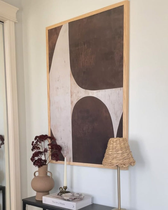 Nature Contours, a brown and cream abstract in a light wood frame, above a console table in a narrow entryway