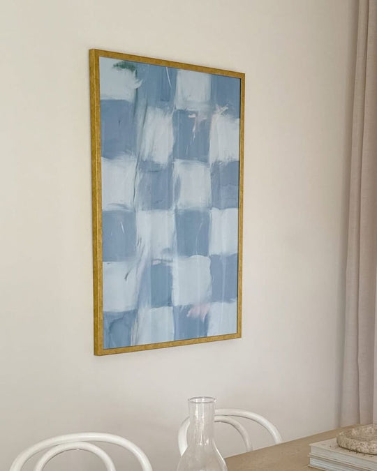 Aqua Checkers, a blue and white checked painting in a gold frame, on a dining room wall above a wooden table