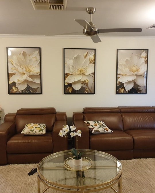 Three framed Gentle Blooms prints above brown leather sofas